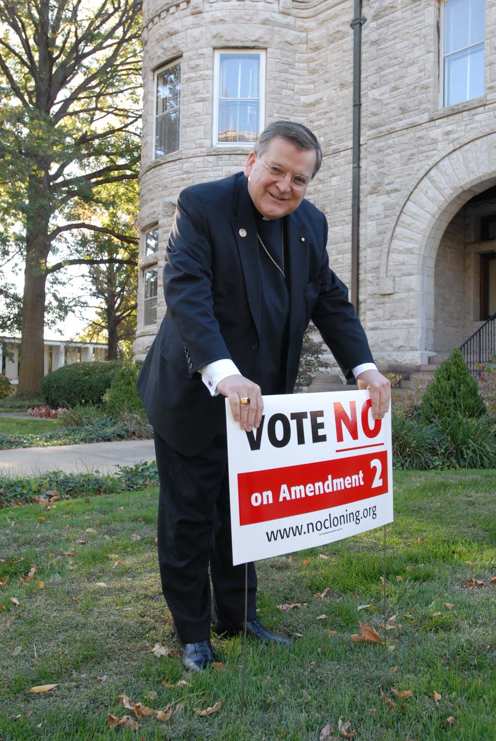 Historical - Photograph - Archbishop Burke with sign in yard of residence regarding Amendment 2, stem cell initiative