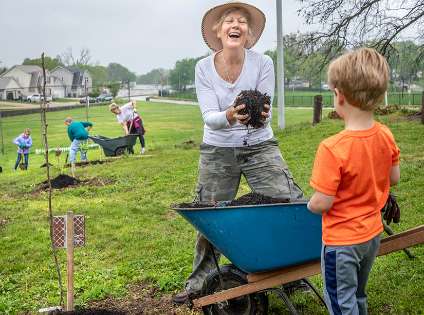 Angie Freshley, a parishioner at Our Lady of the Holy Cross in Baden, laughed at her 3-year-old grandson, Henry Dugan, as they mulched a newly planted tree in the parish’s orchard. Freshley helped spearhead the planting of the orchard as one way to respond to Pope Francis’ call to care for the environment in his encyclical, “Laudato Si’.”