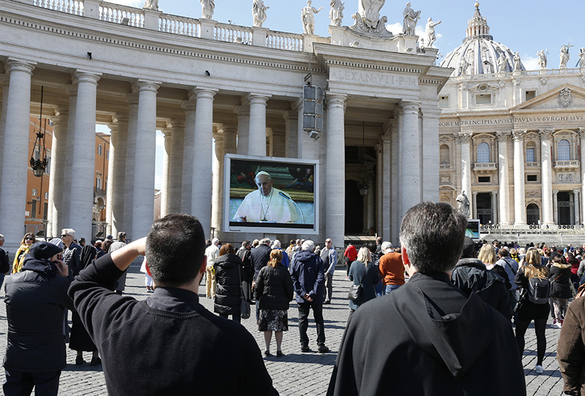 Pope Francis is pictured on a video monitor in St. Peter’s Square as he led the Angelus from his library in the Apostolic Palace at the Vatican March 8. As a precaution to avoid spread of the coronavirus, the pope’s Sunday Angelus was broadcast on television and displayed on monitors in St. Peter’s Square.