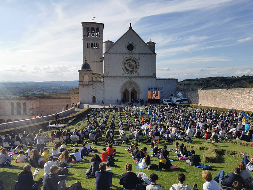 People sat outside the Basilica of St. Francis in Assisi for the beatification Mass of Carlo Acutis in Assisi, Italy, Oct. 10. The Mass was held inside the basilica but measures to prevent the spread of COVID-19 meant that most of the attendees sat outside.