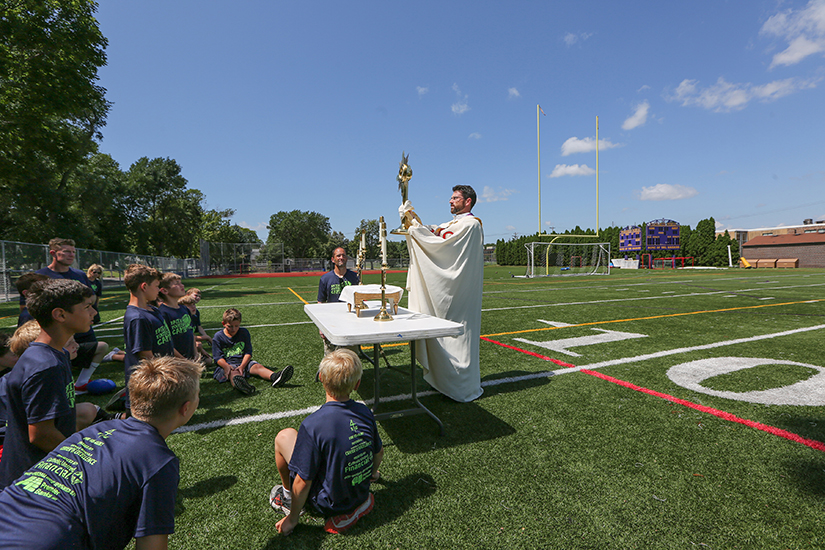 Father Michael Daly held a monstrance with the Eucharist during Faith and Football Camp Aug. 7 at Cretin-Derham Hall High School in St. Paul, Minn. The three-day camp featured football drills and scrimmages mixed in with Mass, Rosary, Stations of the Cross and adoration.