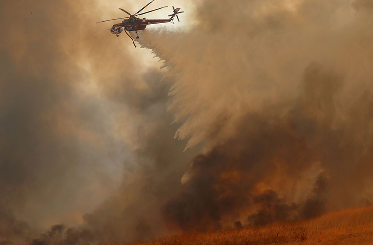 A helicopter dropped water on a fast moving wildfire Oct. 9, 2017 in Orange, Calif. Climate scientists attribute increased fire occurrences in part to warm, dry weather patterns caused by global climate change.