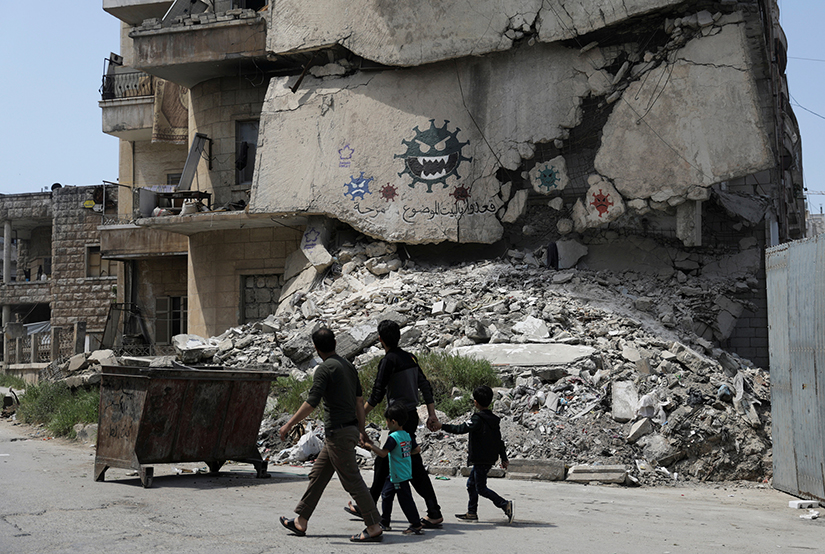People walked past a damaged building depicting drawings alluding to COVID-19 encouraging people to stay at home in Idlib, Syria April, 18.