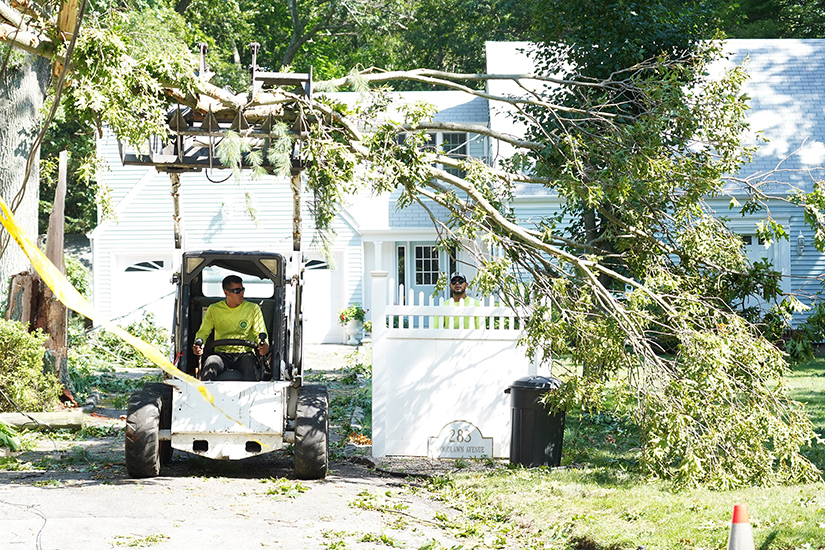 A worker used a front loader with a grapple rake to remove tree limbs from the property of a home in St. James, N.Y., Aug. 5, a day after Tropical Storm Isaias swept through the Long Island community.