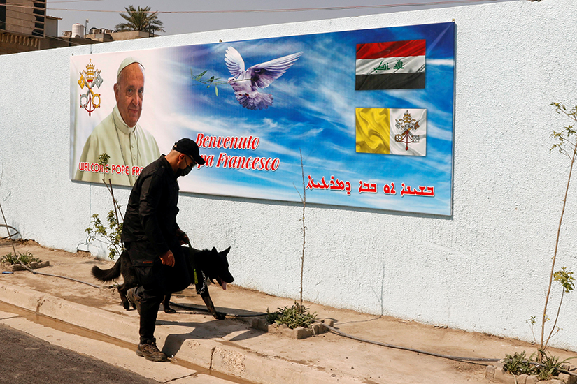 A security officer walked with a dog near a poster of Pope Francis in Baghdad March 3. Pope Francis plans to visit Iraq March 5-8.