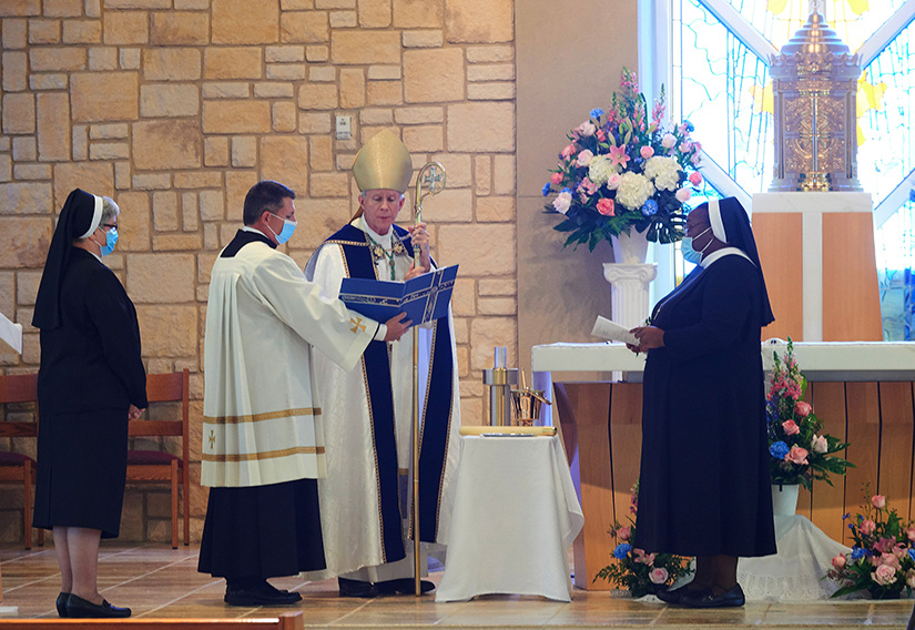 Sister Josephine Garrett, right, stood before Bishop Joseph E. Strickland of Tyler, Texas, Nov. 21, 2020, during the Mass at St. Joseph Vietnamese Catholic Church in Grand Prairie, Texas, where she professed her final vows as a Sister of the Holy Family of Nazareth. Sister Kathleen Maciej, provincial superior of the Holy Family Province of the Sisters of the Holy Family of Nazareth, is standing to the left.