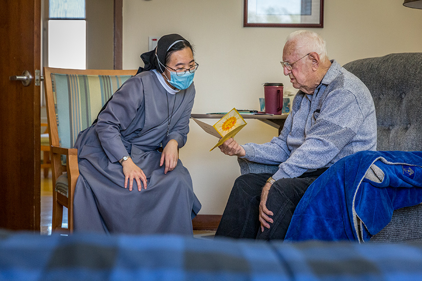Msgr. Jerome Buchheit, who is celebrating his 70th anniversary of ordination on May 3, laughed with Sister Peter Marie Tran as he opened cards from well-wishers at Mother of Good Counsel Home on April 19.