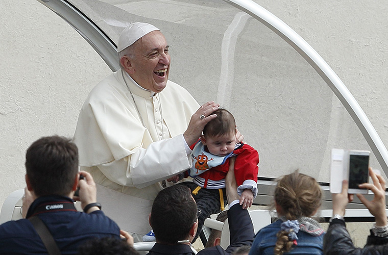 Pope Francis smiled as a papal security guard held up a baby during his general audience in St. Peter’s Square at the Vatican April 18. In his talk, the pope said that the name given at baptism takes the child out of anonymity and is the first step in the journey as a Christian.