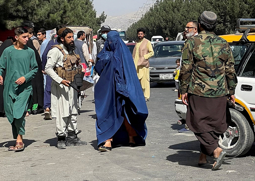 A member of the Taliban forces blocked the roads around Kabul airport as a woman wearing a burqa walks past Aug. 27. Religious minorities and women are concerned about their treatment at the hands of the Taliban and other religious extremists.