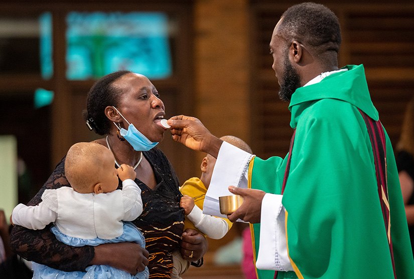 Parishioner Gladys Thuo received Communion from Father Peter Faimega, pastor of St. Norbert Parish, during a Mass in Swahili at the parish in Florissant on Sept. 4. Thuo was at the Mass with her 13-month-old twins Neema and Jonathan Thuo.