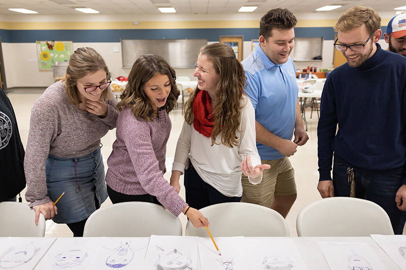 Sisters Maria Edington, center in white, and Clare Hoenig, left of Maria, laughed while looking over hand-drawn images of Friendsgiving attendees with Mary Kullman, left, Jesse Edington, second from right, and Jonathan McCullough on Nov. 17 at St. Joseph School in Josephville.