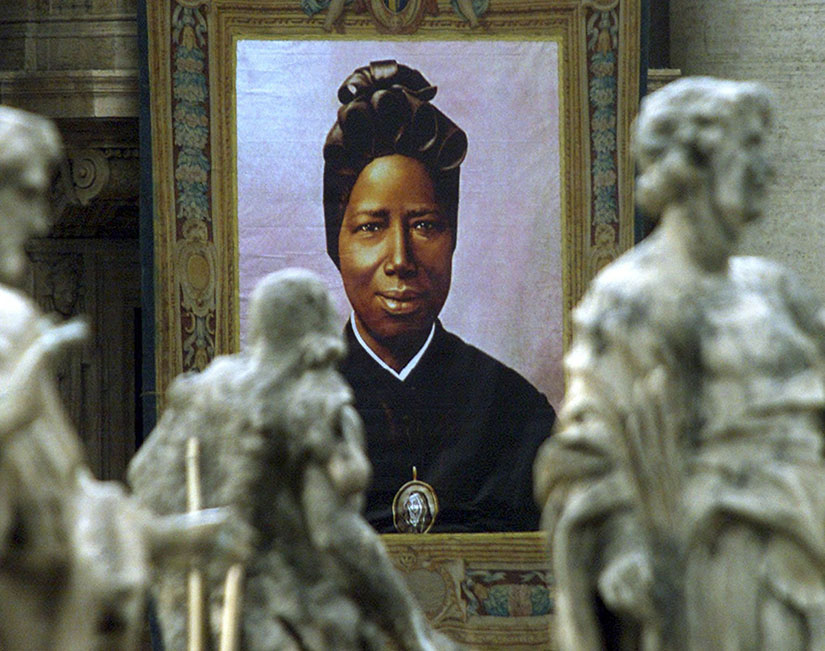 An image of St. Josephine Bakhita, a native of Sudan who was enslaved and later became a nun, hung from the facade of St. Peter’s Basilica Oct. 1, 2000, at the Mass of her canonization. At his audience Oct. 11, Pope Francis said that St. Josephine Bakhita demonstrates how love liberates people from oppression and frees them to forgive their oppressors and break cycles of hatred and violence.