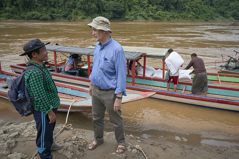 Maryknoll Father John Barth, a missionary from the United States, talked with Pah Kler, a Burmese Catholic catechist, as rice is loaded on boats in Mae Sam Laep, a Thai village on the Salween River, Sept. 29, 2022. Kler was supervising the movement of food and other humanitarian supplies to internally displaced families hiding in the forests of Myanmar.