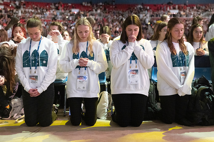 From left, Taylor Birkenmeier, Bella Obert, Abby Schultz and Rose Juergensmeyer knelt during the communion procession of the opening Mass of SEEK24 on Jan. 1 at America’s Center Convention Complex in St. Louis. Obert attends Rockhurst University in Kansas City, the others are students at Lindenwood University.